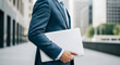 © Dropflare - Businessman in blue suit holding slim laptop in city district area