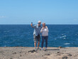 © luciano - Senior couple enjoying retirement vacation, smiling and taking a selfie with smartphone on a sunny day at the ocean coastline, capturing happy memories together