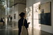 © maikuto - Woman observing abstract artwork inside a contemporary art gallery with natural light creating elegant shadows across the exhibition space.