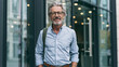 © CreativeArt - Senior businessman smiling, standing confidently outside a modern office building, depicting professionalism and experience