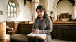 © Keo - A woman sits in a church pew, holding an open Bible and praying. She is wearing a cardigan and jeans.