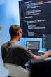 © SAT65 - Male Software Engineer Typing During a Focused Coding, Working on Technical Tasks with Code Displayed on Screen Sitting at Desk In Tech Office. Male Programmer Working on a Development Project.