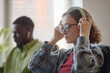 © TrueFrame Collective - Young adult Caucasian woman adjusting headphones while working beside Black man in office. Depicting focused teamwork and audio communication for workplace training or tech support