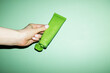 © Colour Laboratory/Stocksy - Hand holding a cosmetic beauty product green tube with lid with flash