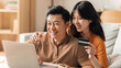 © Prostock-studio - Happy Asian Couple In Their 30s Smiling And Shopping Online Together At Home, Sitting On Sofa With Laptop And Credit Card, Enjoying Convenient Online Shopping Experience, Home Office Concept.