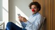 © Ariestia - Smiling Young Businessman Wearing a Red Clown Nose While Using a Smartphone in a Modern Office Setting