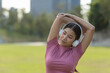 © Ratirat - Relaxed young asian woman with headphone stretching her arm before exercise in park. She enjoys listening to music for healthy lifestyle, feeling calm and content