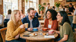 © Celt Studio - Happy diverse group of young friends laughing while sitting around wooden table drinking fresh coffee inside modern cozy cafe enjoying pleasant conversation