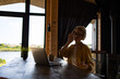 © Sofiia Shunkina - A Caucasian woman with curly hair and glasses wearing headphones and a yellow shirt is enjoying music while working on her laptop at a wooden table