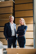 © Westend61 - Smiling senior businessman with colleague standing in front of stacked wood