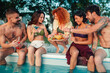 © Zamrznuti tonovi - Group of friends sharing fruit and drinks by the pool on a summer day, enjoying a relaxing vacation party