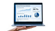 © unairakstudio - A hand holding a crisp laptop screen showing a clean and organized financial analytics dashboard, white background.