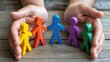 © Azman - Human hands cupping a row of colorful wooden human figures on a textured wooden surface symbolizing teamwork diversity inclusion and corporate social responsibility