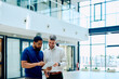 © we.bond.creations - Two diverse businessmen collaborating on a project, analyzing data on a tablet in a contemporary office setting, sharing ideas