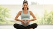 © Erisna Yolanda - Pregnant woman sitting cross-legged making heart shape.
