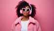 © Vadym - Young woman with afro hair wears pink headphones and sunglasses. She models a fluffy pink jacket over white top against a pink backdrop. Her style is modern and vibrant.