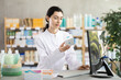 © JackF - Qualified female pharmacist holds a box of pills in her hands and stands near a computer in a pharmacy. Pharmacist puts pills and medicines behind the counter