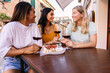© Xavier Lorenzo - Multiracial female friends enjoying red wine at cafe table. Young women sharing laughter and conversation in Italy. Lifestyle and social concept.