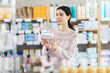 © JackF - Young woman standing near shelves with medicines and choosing boxes of pills and supplements in a European pharmacy