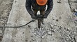© SimpleDesignStudio - Construction worker using a pneumatic jackhammer to break concrete pavement on a road renovation site