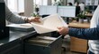 © Authenticlens - Two professional office workers exchanging important paper documents near a metal filing cabinet in workplace
