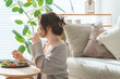 © buritora - A stylish young Asian woman eating at the living room table.