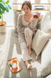 © buritora - A stylish Asian woman relaxing on a living room sofa during teatime.