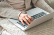 © buritora - A woman's hands as she sits on her sofa at home and looks at her computer.