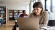 © Eve - Happy young woman looking at laptop screen in university library studying for exams online education female student learning lesson college classroom academic research digital knowledge