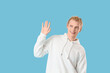 © Pixel-Shot - Young blonde man in white hoodie waving hand on blue background