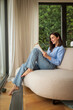 © gzorgz - Relaxed woman reading a book while sitting on a comfortable sofa at home