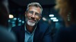 © The Little Hut - Smiling mature businessman in a suit with glasses, engaged in a business meeting with colleagues