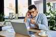 © LIGHTFIELD STUDIOS - A handsome african american man is deep in thought while working at his laptop in a modern office setting.