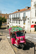 © Alberto - Pink tuk tuk parked on a steep cobblestone street in lisbon, portugal, on a sunny day