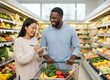 © KIMOG - Happy African American Man Looking at Asian Woman Holding Notebook While Grocery Shopping