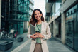 © Zamrznuti tonovi - Smiling businesswoman holding laptop and coffee, walking in modern city, confident and successful career woman outdoors