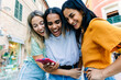 © Xavier Lorenzo - Happy young women checking smartphone together outdoors. Friends sharing digital moments while traveling in a European city. Technology and lifestyle concept.