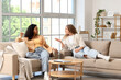 © Pixel-Shot - Two young women chatting on sofas in a bright living room