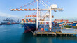 © Yellow Boat - gantry cranes loading cargo container ship at a busy commercial port terminal, with trailer trucks lined up on the dock to support global maritime logistics and supply chain operations.