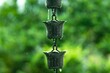 © Kakabe - Raindrops cascading from decorative metal fixtures surrounded by lush greenery create a tranquil atmosphere, highlighting the beauty of nature and the soothing sound of rain