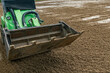 © kalyanby - Mini loader levelling quartz sand surface on equestrian arena outdoor horse riding ring footing installation and maintenance process