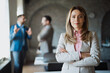 © Novak - Professional business woman posing at the workplace with team behind her.