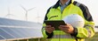 © hubaib - Man in safety gear examines tablet near solar panels and wind turbines