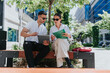 © qunica.com - Two business colleagues sit on a bench reviewing a tablet and papers while discussing work. The pair collaborate outdoors in an urban setting during a casual business meeting.