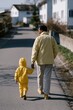 © Andrii Zastrozhnov - Father and child holding hands walking down a residential street in yellow jackets for family lifestyle background and parenting banner