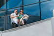 © qunica.com - Two business associates review documents and a tablet while standing on an office balcony. They discuss paperwork and digital files outside a modern glass building.