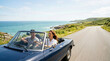 © Xenia - Happy couple driving a blue convertible car on a coastal road. Man and woman enjoying a summer road trip along the ocean. Vacation and travel lifestyle concept