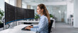 © itlada - Female software developer coding on multiple monitors in a bright modern corporate office, featuring dark mode programming interfaces for technology industry and IT professional career concepts
