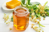Sweet honey in glass jar, honeycomb and linden flowers on white wooden table, closeup
