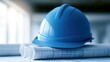 © Neon Stock - Blue construction hard hat resting on architectural blueprints